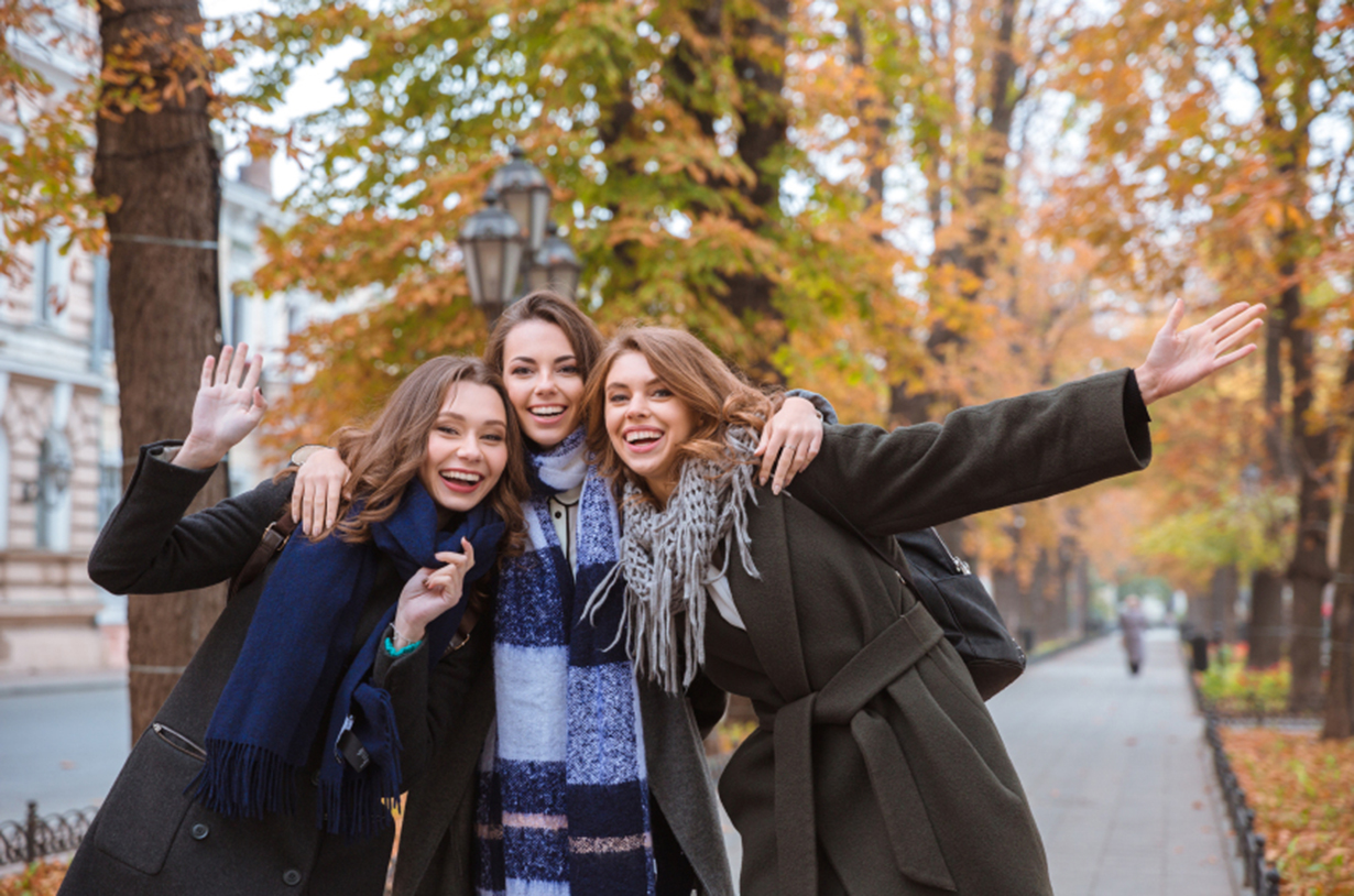 Portrait of a three happy women standing together in autumn park and looking at camera